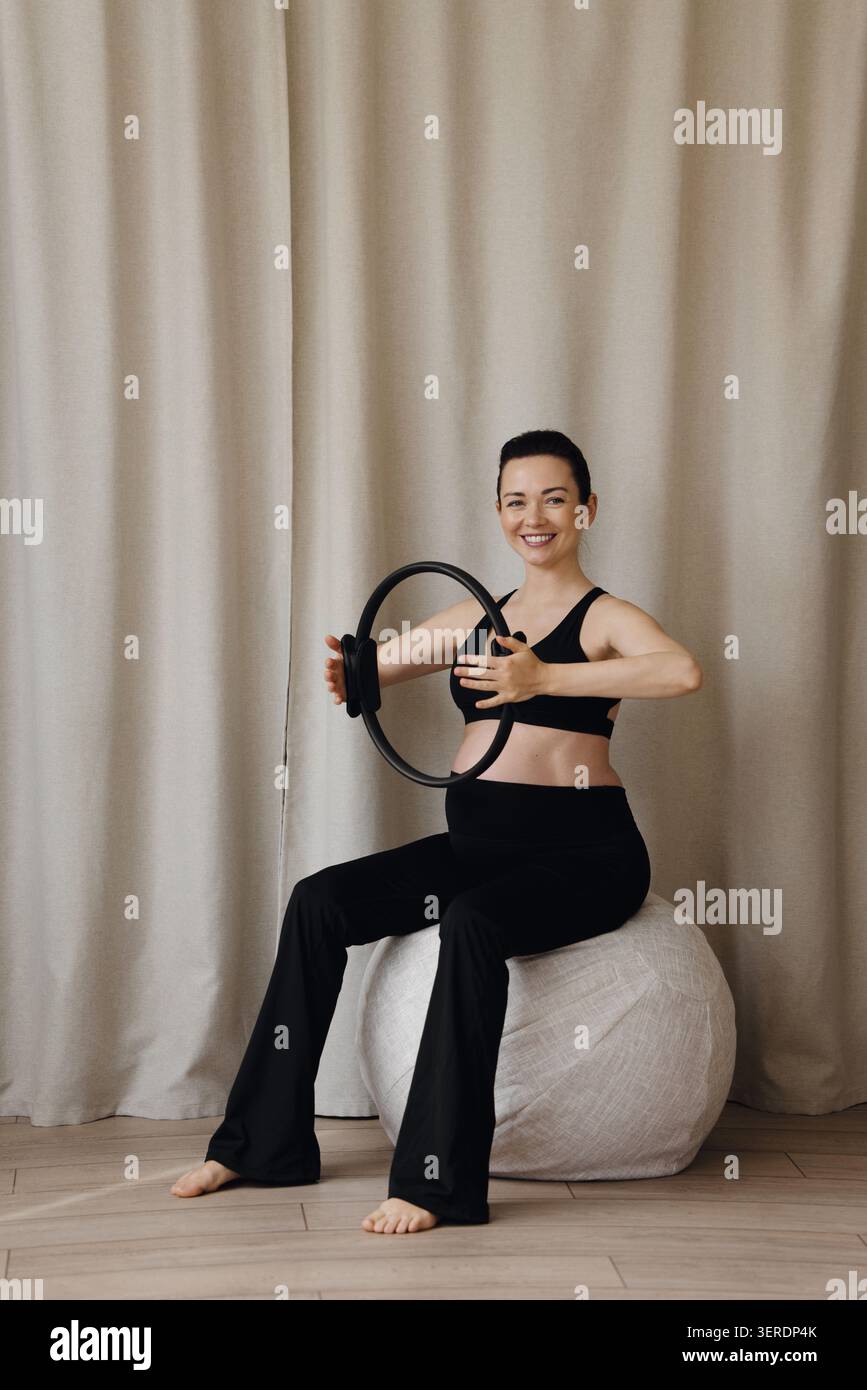 Femme enceinte assise sur le ballon de fitness tenant l'anneau de pilates pendant l'entraînement prénatal Banque D'Images