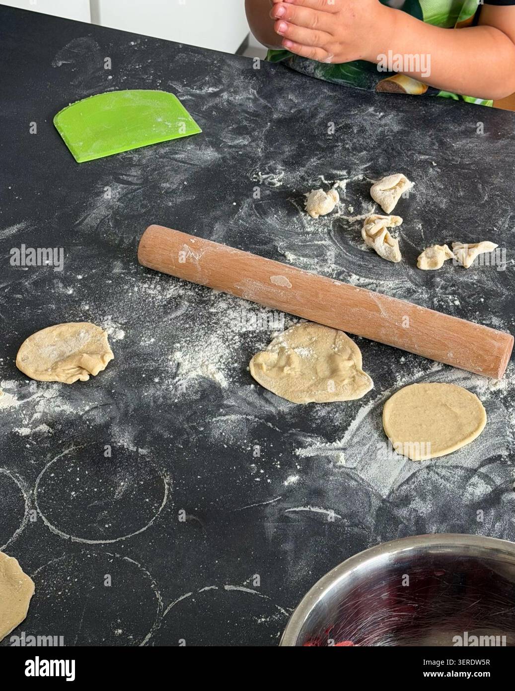 Mains de l'enfant préparant la pâte avec un rouleau à pâtisserie sur un comptoir noir, entouré de farine Banque D'Images