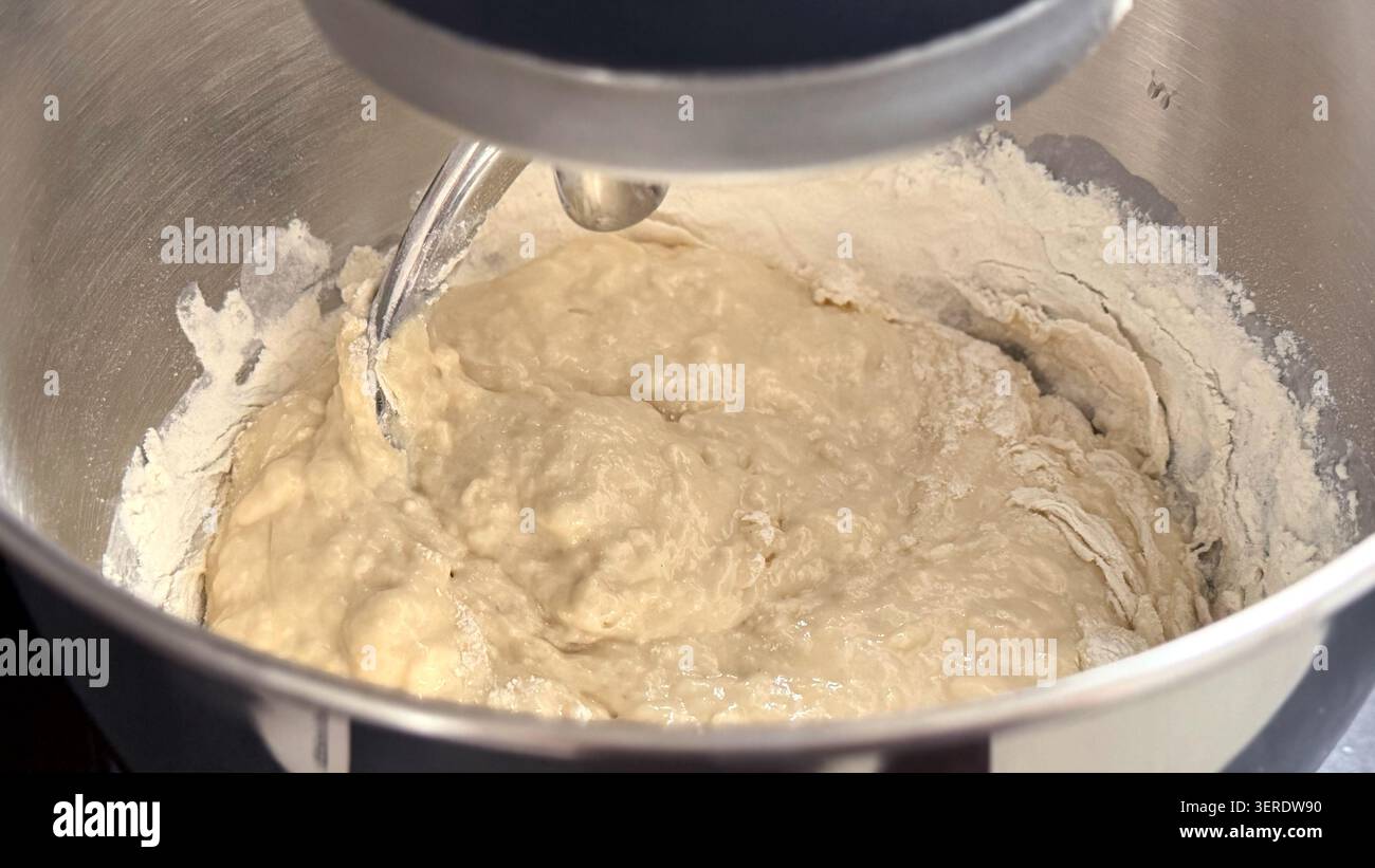 Mélange de pâte dans un bol en acier inoxydable préparé avec un batteur sur pied, montrant la farine et les ingrédients humides se mélangeant ensemble pour la cuisson Banque D'Images