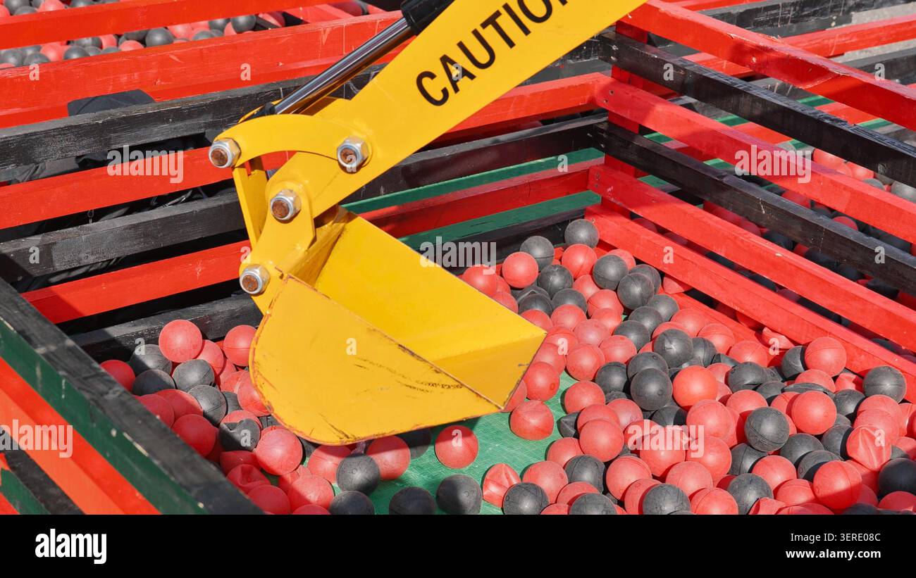 Bras d'excavatrice jaune industriel dans un jeu de fosse à boule rouge et noire. Banque D'Images
