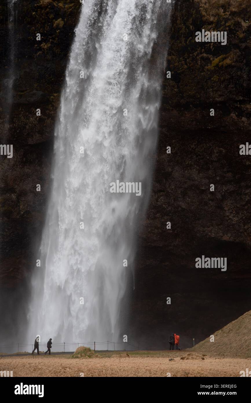 Cascade Seljalandsfoss descendant la falaise, avec des gens debout à sa base, soulignant l'immense échelle et la beauté naturelle de l'islande. Glace Banque D'Images