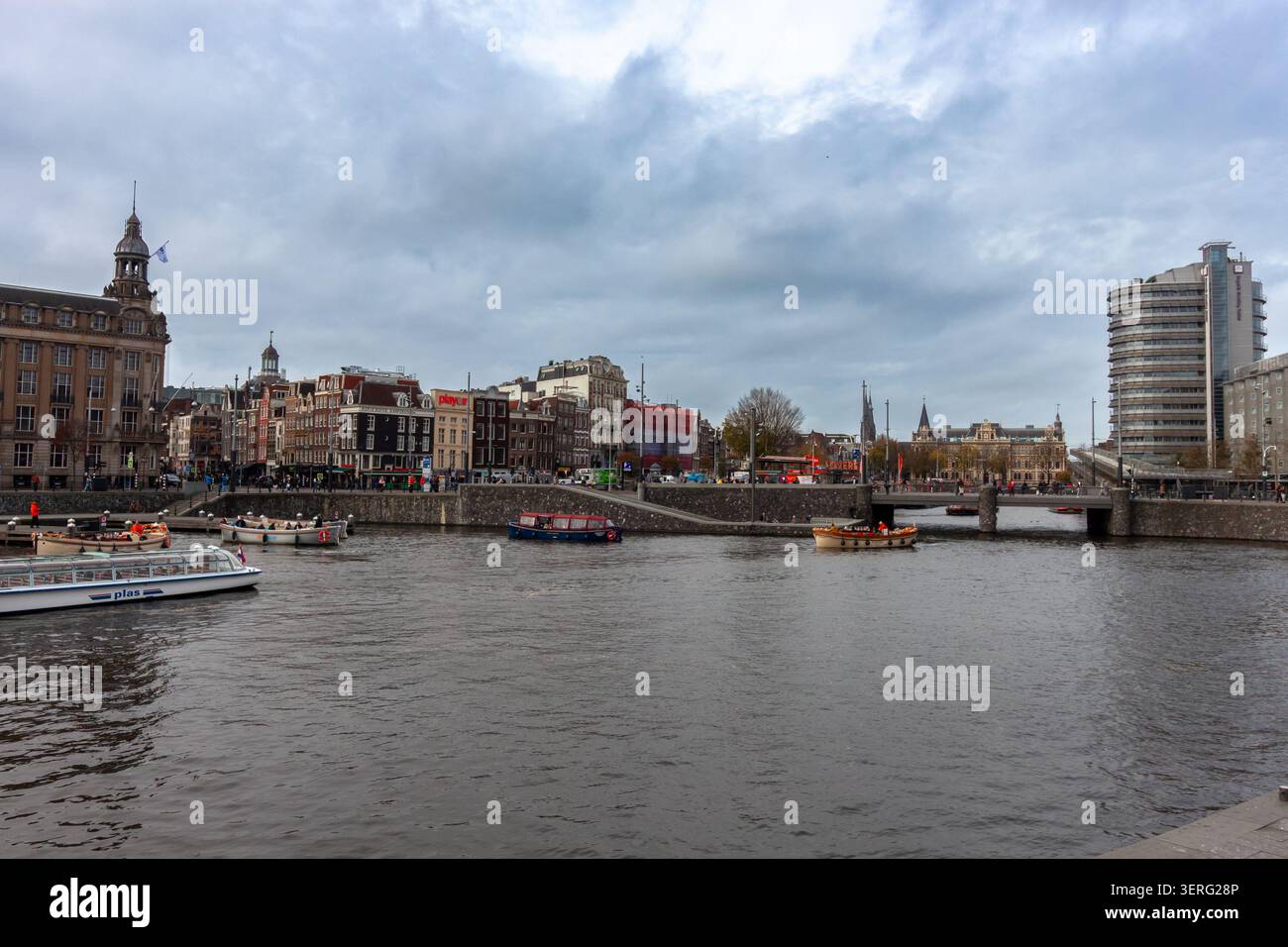 AMSTERDAM, PAYS-BAS - 10 NOVEMBRE 2025 : paysage urbain pittoresque du front de mer d'Amsterdam avec des bateaux d'excursion sur la rivière sous un ciel nuageux spectaculaire Banque D'Images