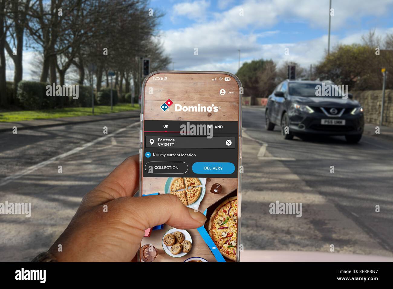 Main tenant smartphone affichant l'application de Domino pour la livraison de pizza avec la route en arrière-plan Banque D'Images