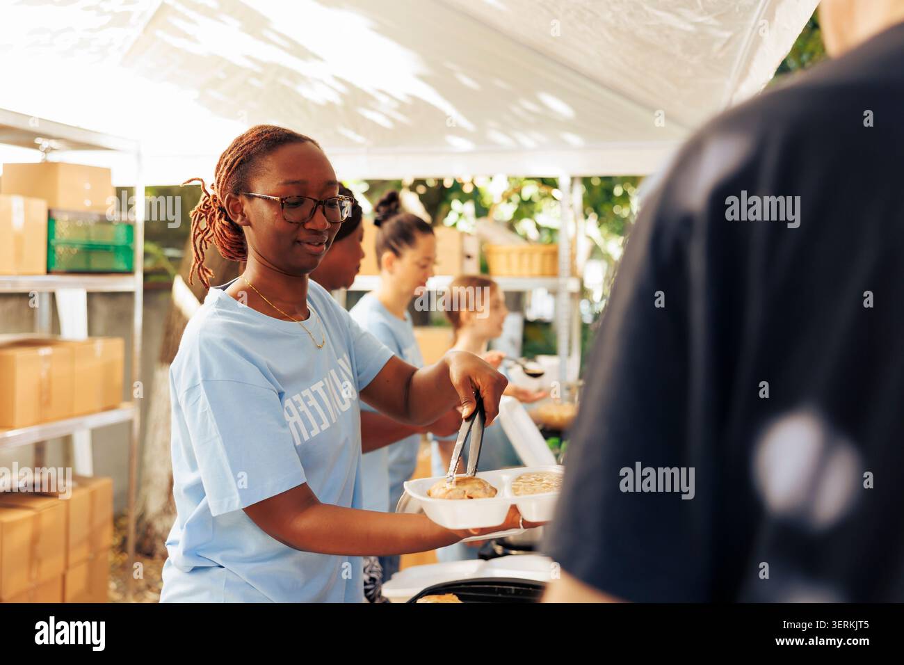 Femme afro-américaine servant de la nourriture gratuite aux pauvres et nécessiteux individus dans une banque alimentaire extérieure. Des femmes bénévoles nourrissant et apportant un soutien aux personnes affamées et moins privilégiées dans un refuge pour sans-abri. Banque D'Images