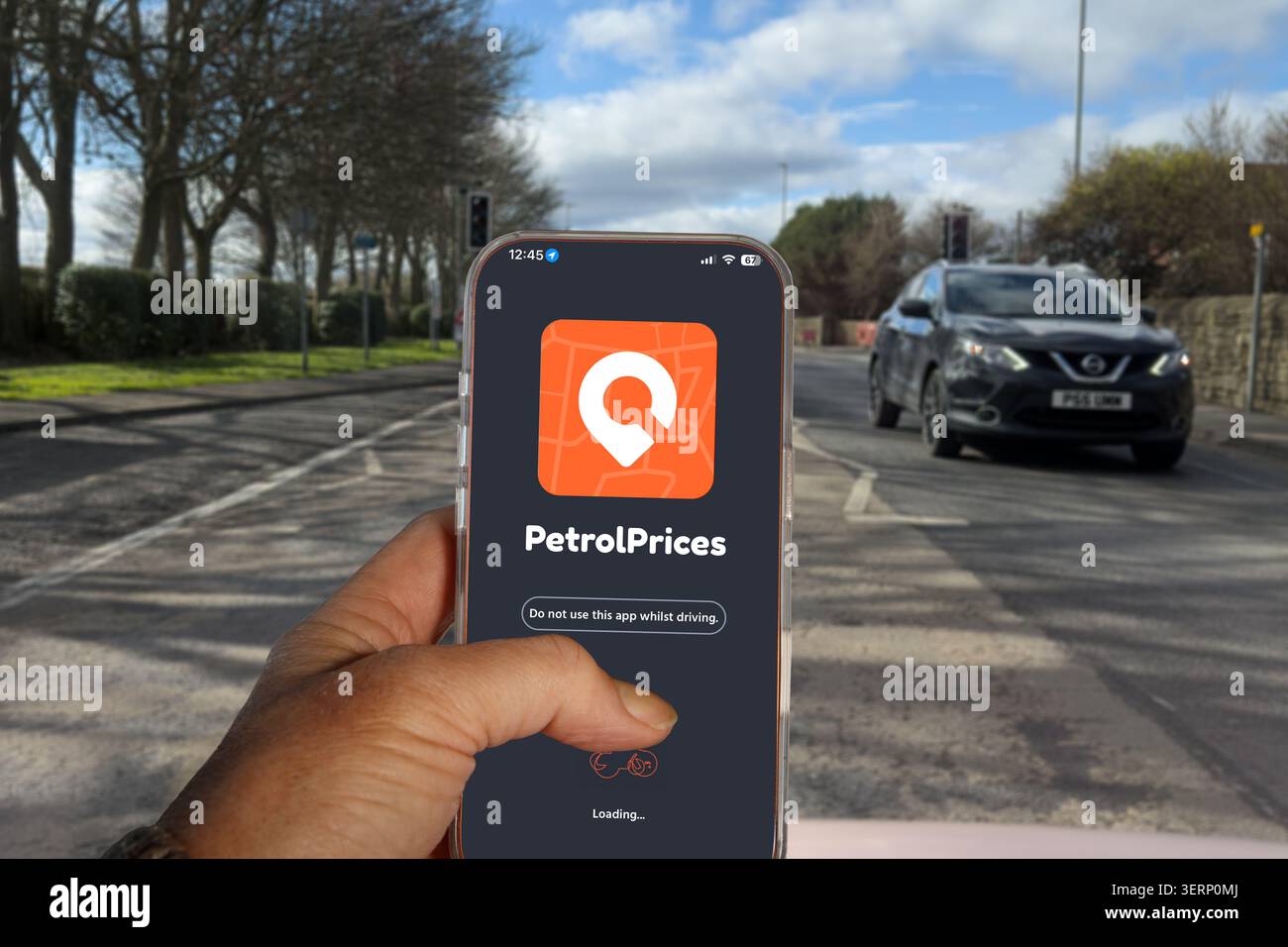 Main tenant iPhone affichant l'application PetrolPrices au Royaume-Uni avec un Nissan Qashqai sur la route en arrière-plan Banque D'Images