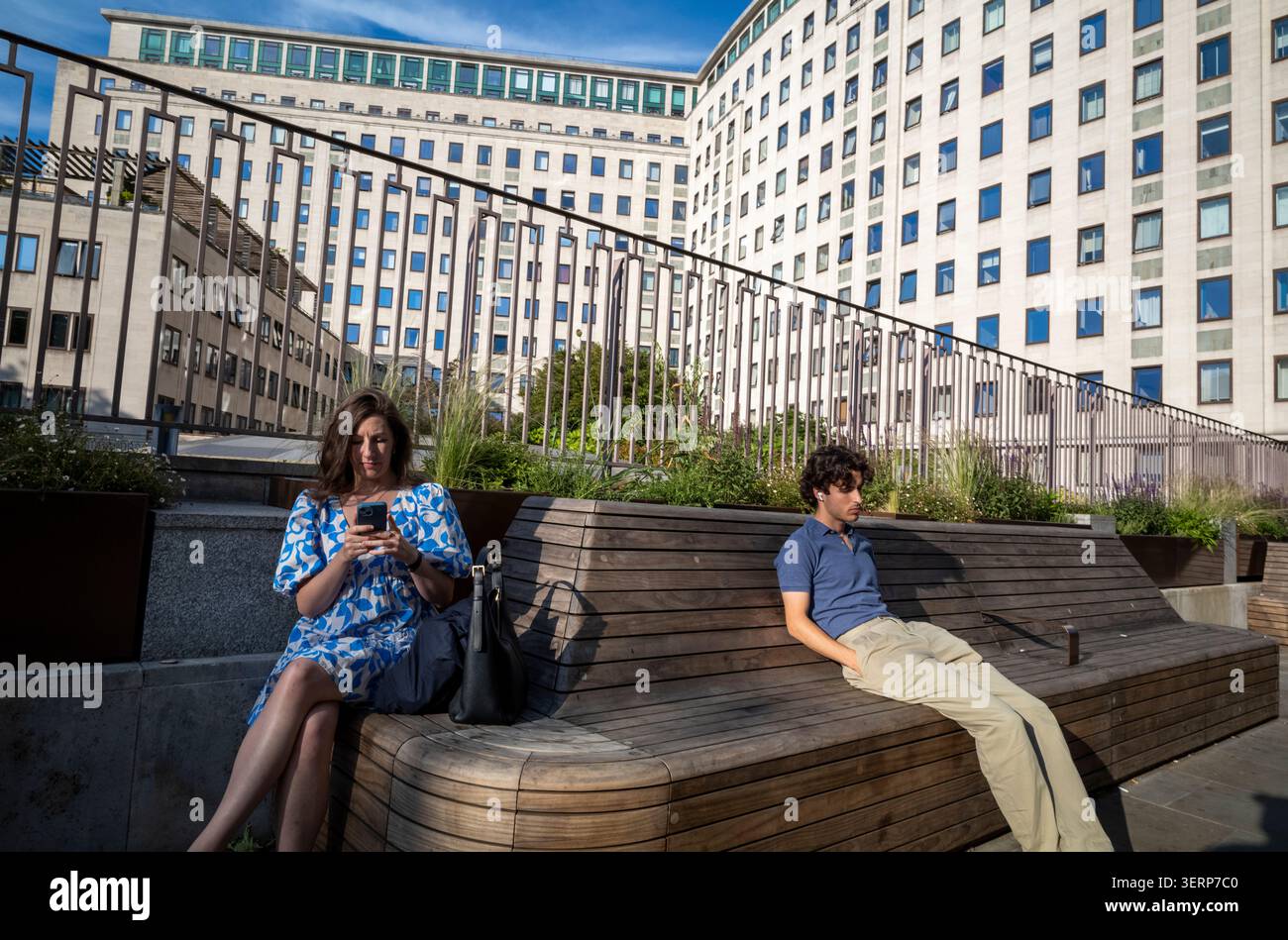 Un jeune homme est assis sur un banc à côté d'une femme immergée dans son smartphone dans le quartier Southbank de la capitale Londres, Angleterre, Royaume-Uni Banque D'Images