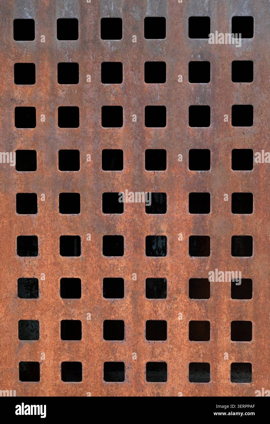 Gros plan vertical d'une surface métallique rouillée altérée avec une grille de découpes carrées, d'ouvertures sombres, de corrosion piquée, de texture oxydée Banque D'Images