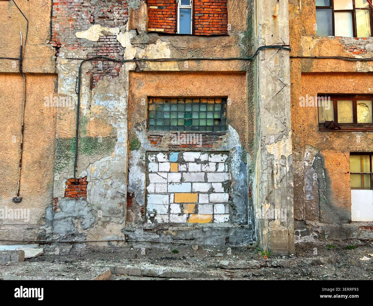 Façade en plâtre pelable d'un bâtiment industriel abandonné avec vieille fenêtre bloquée et brique apparente Banque D'Images