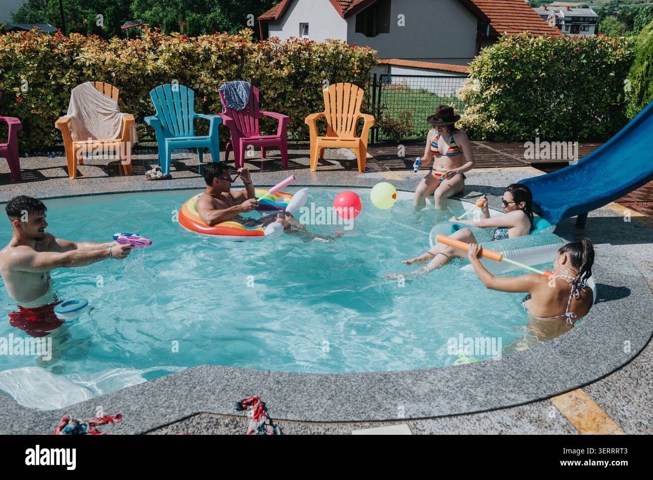 Amis profitant d'une journée d'été à la piscine avec flotteurs, jouets aquatiques et chaises de piscine détendues Banque D'Images