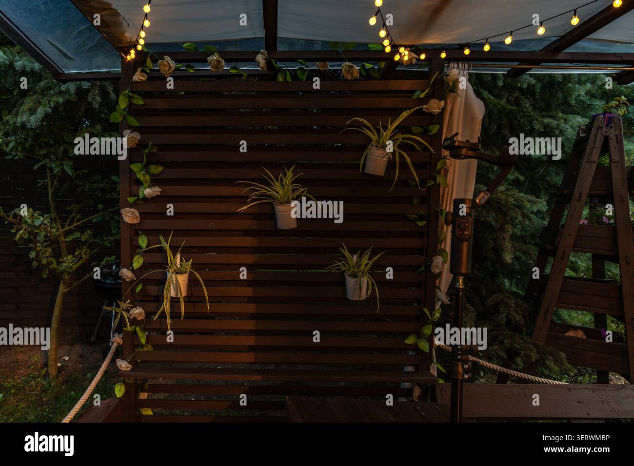 Ambiance chaleureuse en soirée avec guirlande lumineuse LED suspendue sur la terrasse du jardin. L'éclairage doux crée une atmosphère extérieure accueillante, Banque D'Images