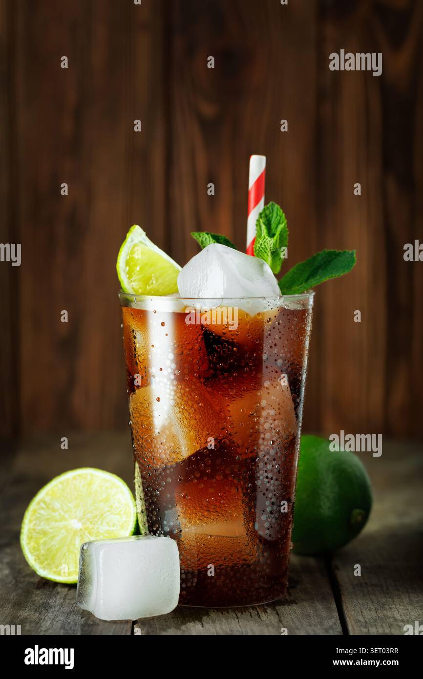 Cuba cocktail libre avec rhum, cola, citron vert frais et menthe en verre avec de la glace sur fond de bois Banque D'Images