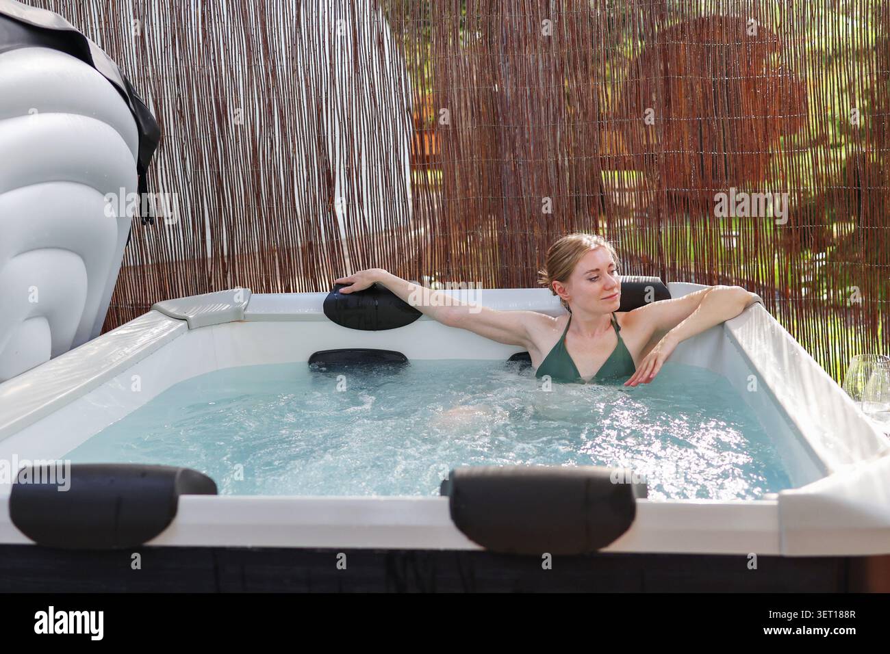 Jeune femme se relaxant dans un bain à remous dans un complexe de glamping de luxe, profitant du bien-être, du confort et d'une retraite paisible dans la nature. Banque D'Images