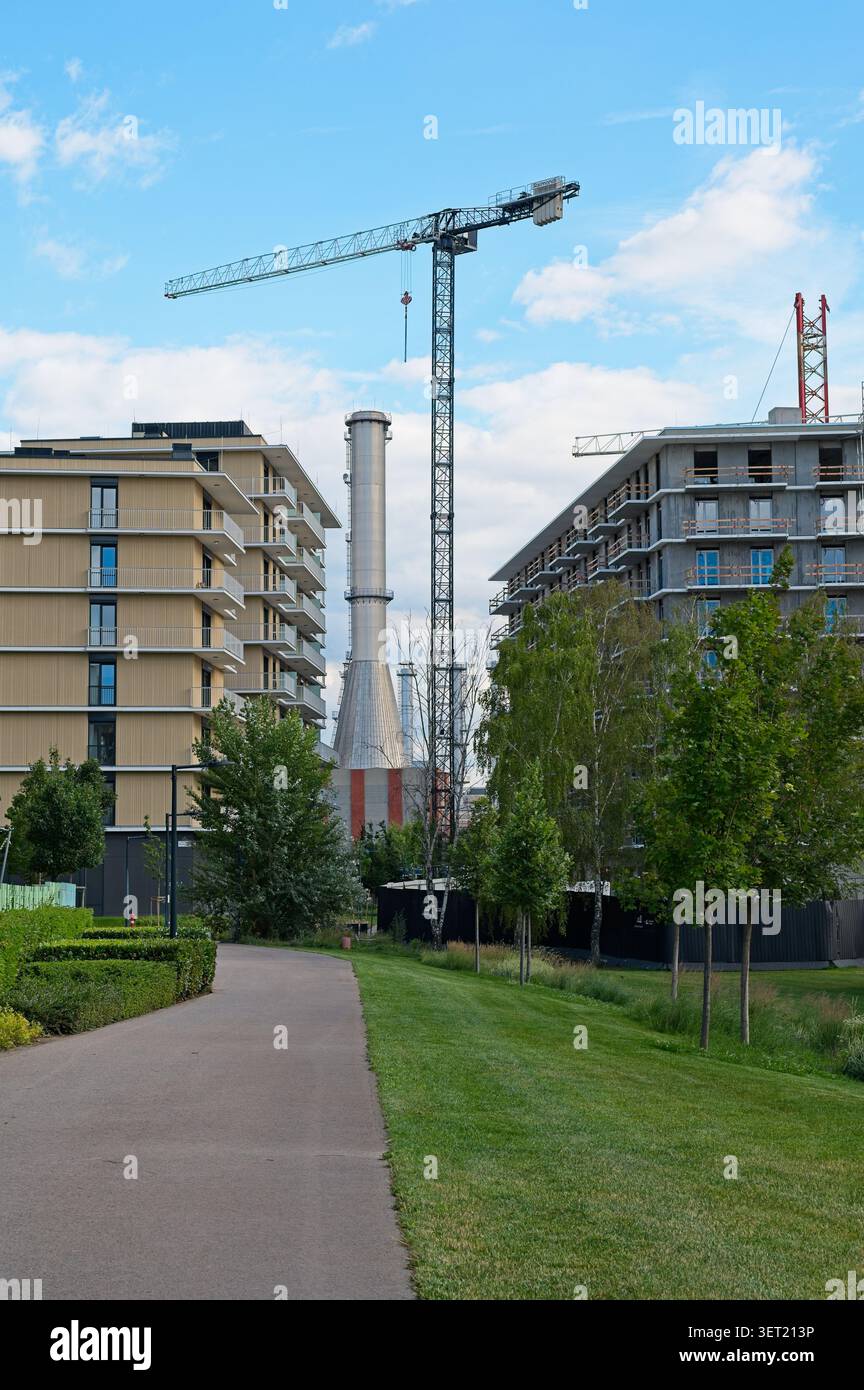 Budapest, Hongrie - 12 juin 2026 : chantier de construction dans le quartier Budapart avec des bâtiments résidentiels modernes, des grues à tour et une cheminée industrielle. Banque D'Images