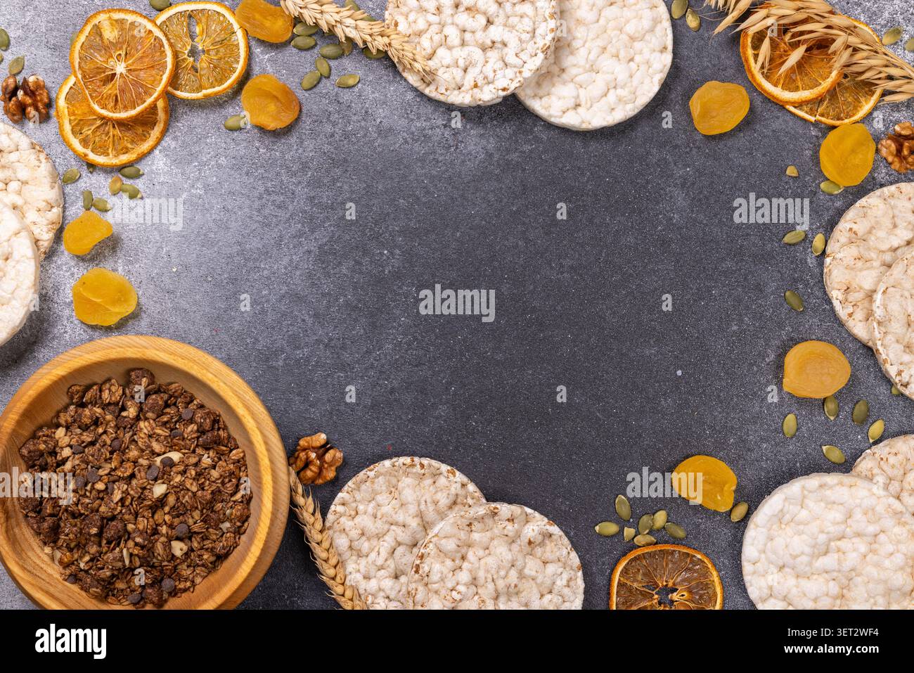 Ingrédients sains du petit déjeuner, y compris granola dans un bol en bois, gâteaux de riz, oranges séchées, abricots, graines de citrouille, et des noix, disposées sur un sombre Banque D'Images