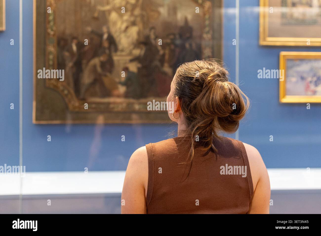 Une personne se tient devant un grand tableau dans un musée d'art. Le visiteur est concentré sur l'œuvre d'art. L'exposition est bien éclairée et comporte plusieurs cadres Banque D'Images
