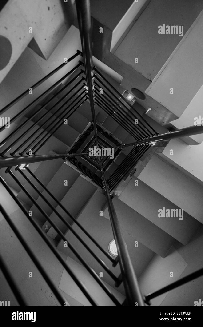 Perspective abstraite noire et blanche descendante d'un escalier en colimaçon carré avec des lignes nettes et des motifs géométriques. Banque D'Images