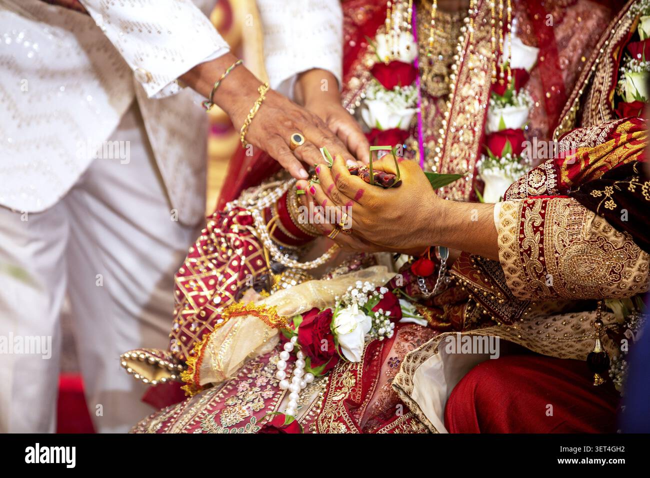 Gros plan des mains d'une mariée et d'un marié participant à un rituel sacré lors d'un mariage indien, orné de bijoux et de vêtements traditionnels Banque D'Images