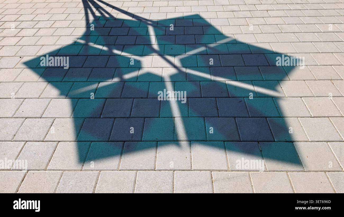 Une ombre sombre symétrique formant un motif étoilé à six pointes s'étend sur un trottoir pavé sous la lumière du soleil de l'après-midi Banque D'Images