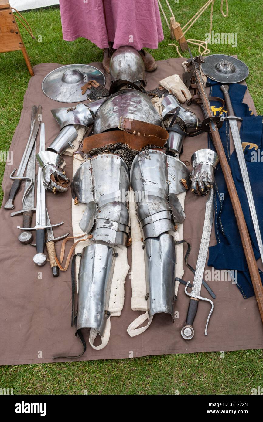 Un costume médiéval complet d'armure plaquée avec casque, gants et épées disposés sur un tissu lors d'une exposition de reconstitution historique en plein air Banque D'Images