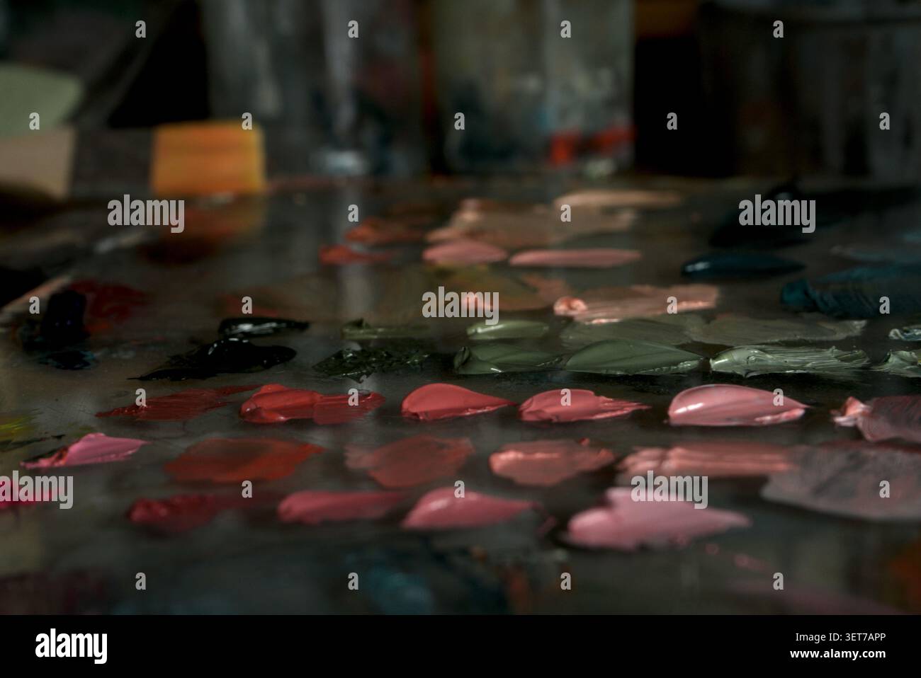 Gros plan d'une palette de peintres à l'huile de verre avec une peinture mixte rose et verte. Banque D'Images