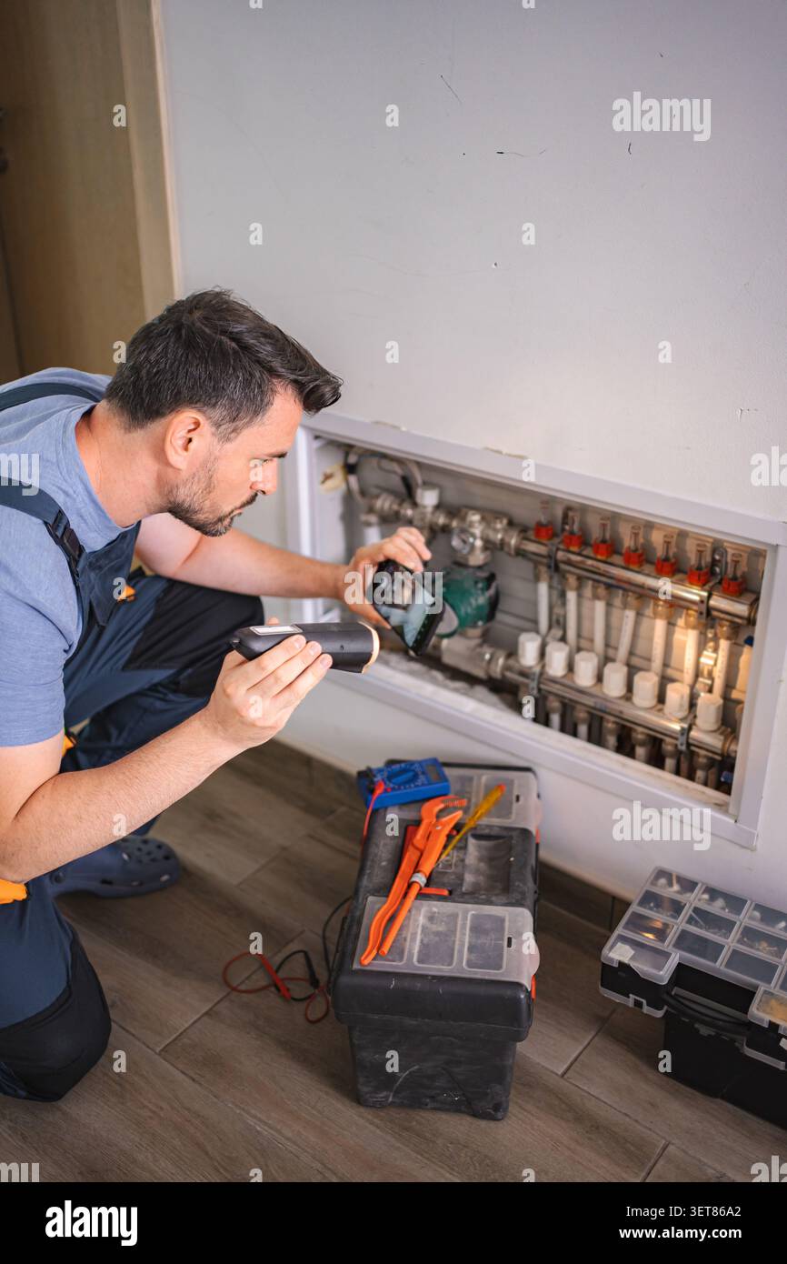 Technicien inspectant le système de chauffage avec lampe de poche et smartphone Banque D'Images
