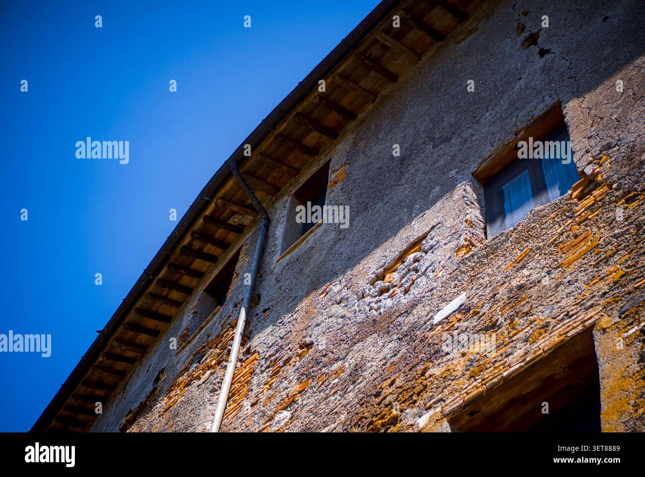 22-05-2023 Italie : fenêtres rustiques sur un mur de briques apparentes avec ciel bleu Banque D'Images