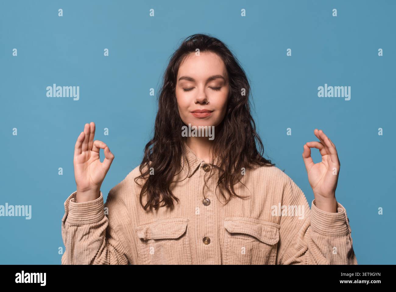 Jeune femme méditant avec les yeux fermés sur fond bleu, concept Mindfulness Banque D'Images