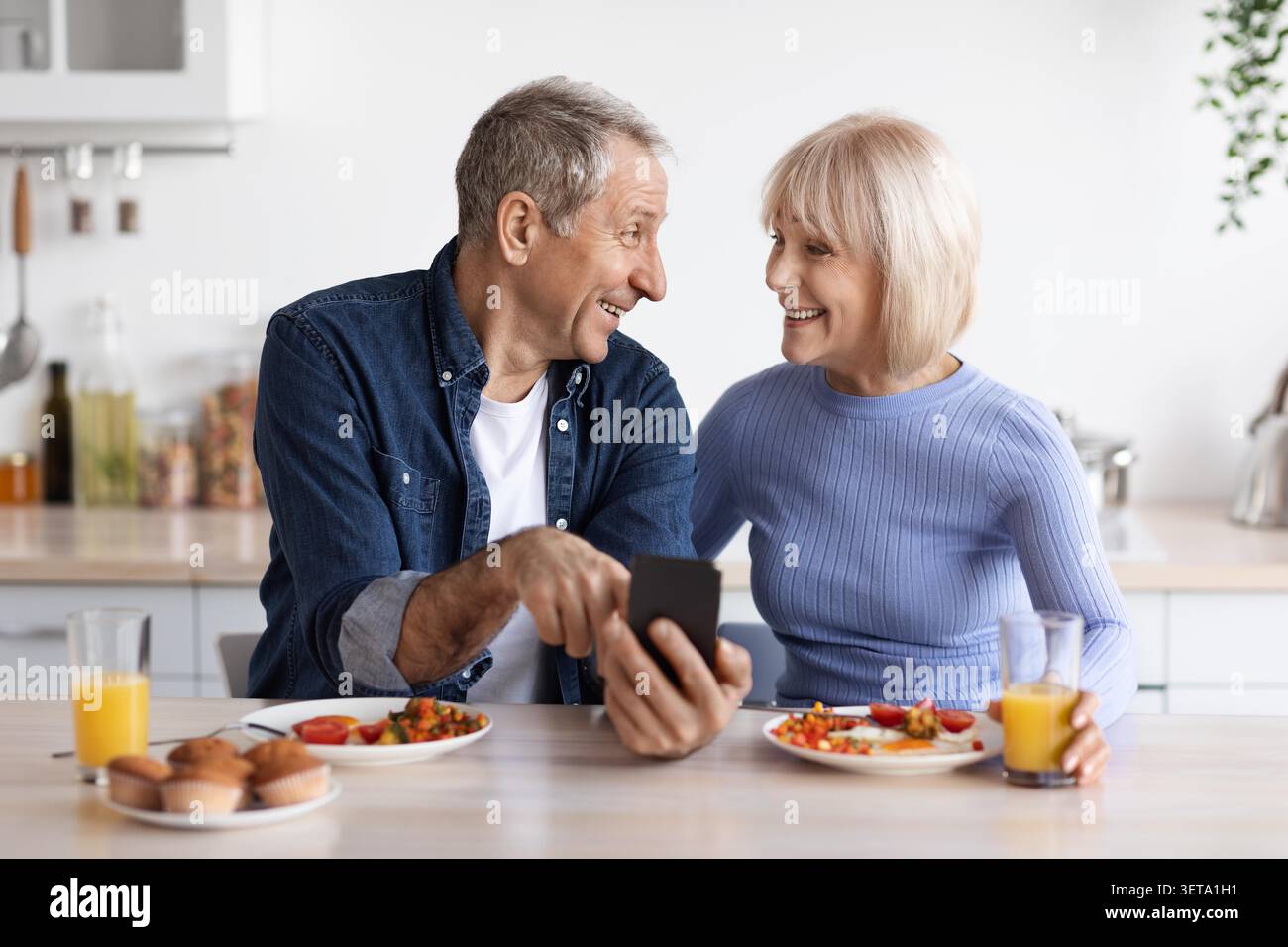 Heureux couple âgé caucasien mangeant le petit déjeuner ensemble à la maison, moment de partage Banque D'Images