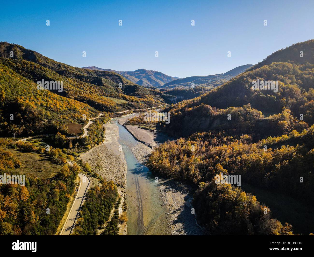 Une perspective aérienne capture une rivière sinueuse qui coule à travers une vallée flanquée de collines ondulantes couvertes d'un feuillage automnal vibrant. Un étroit ro pavé Banque D'Images