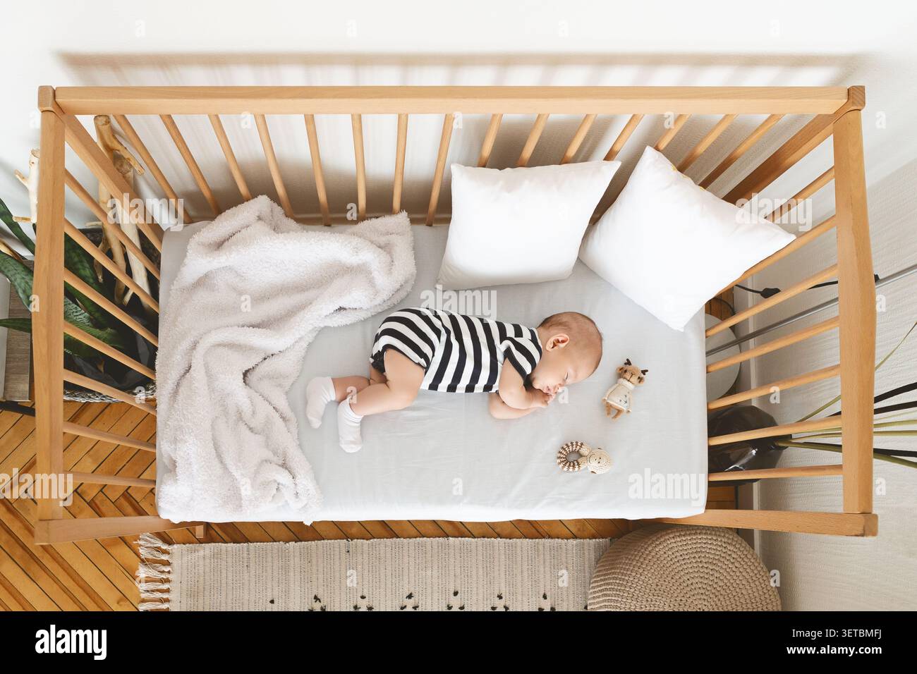 Bébé dormant paisiblement dans un berceau élégant orné de jouets en peluche et d'une literie douce pendant la journée Banque D'Images
