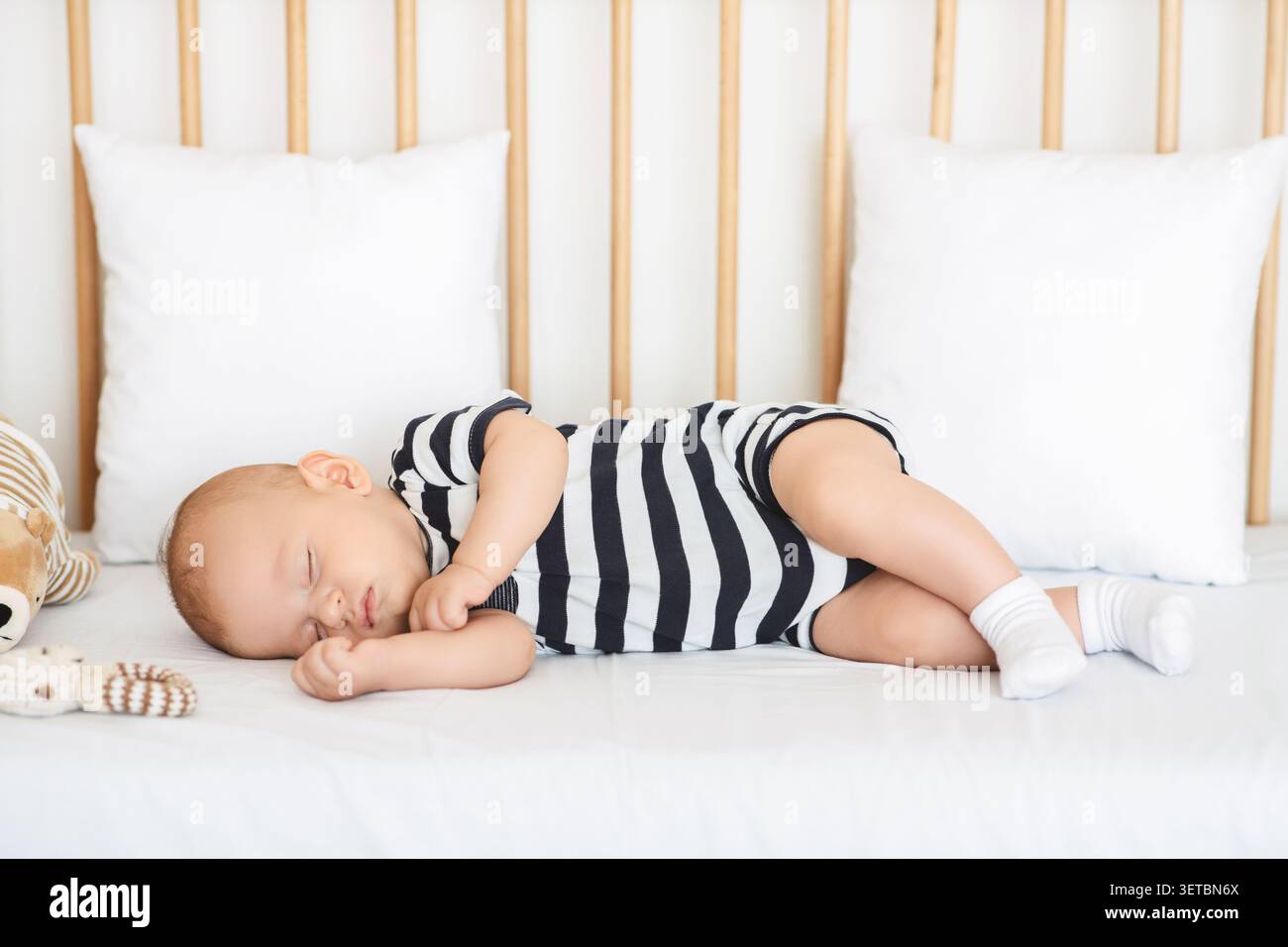 Bébé dormant paisiblement dans un berceau sur un matelas moelleux avec des jouets en peluche à proximité pendant la journée Banque D'Images