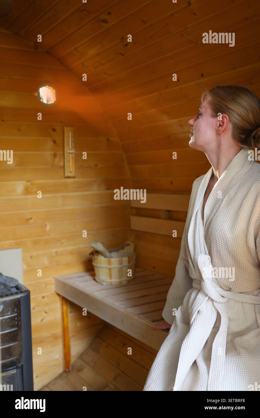 Femme dans un peignoir se relaxant dans un sauna traditionnel en bois, profitant d'une expérience de bien-être paisible et d'auto-soins. Banque D'Images