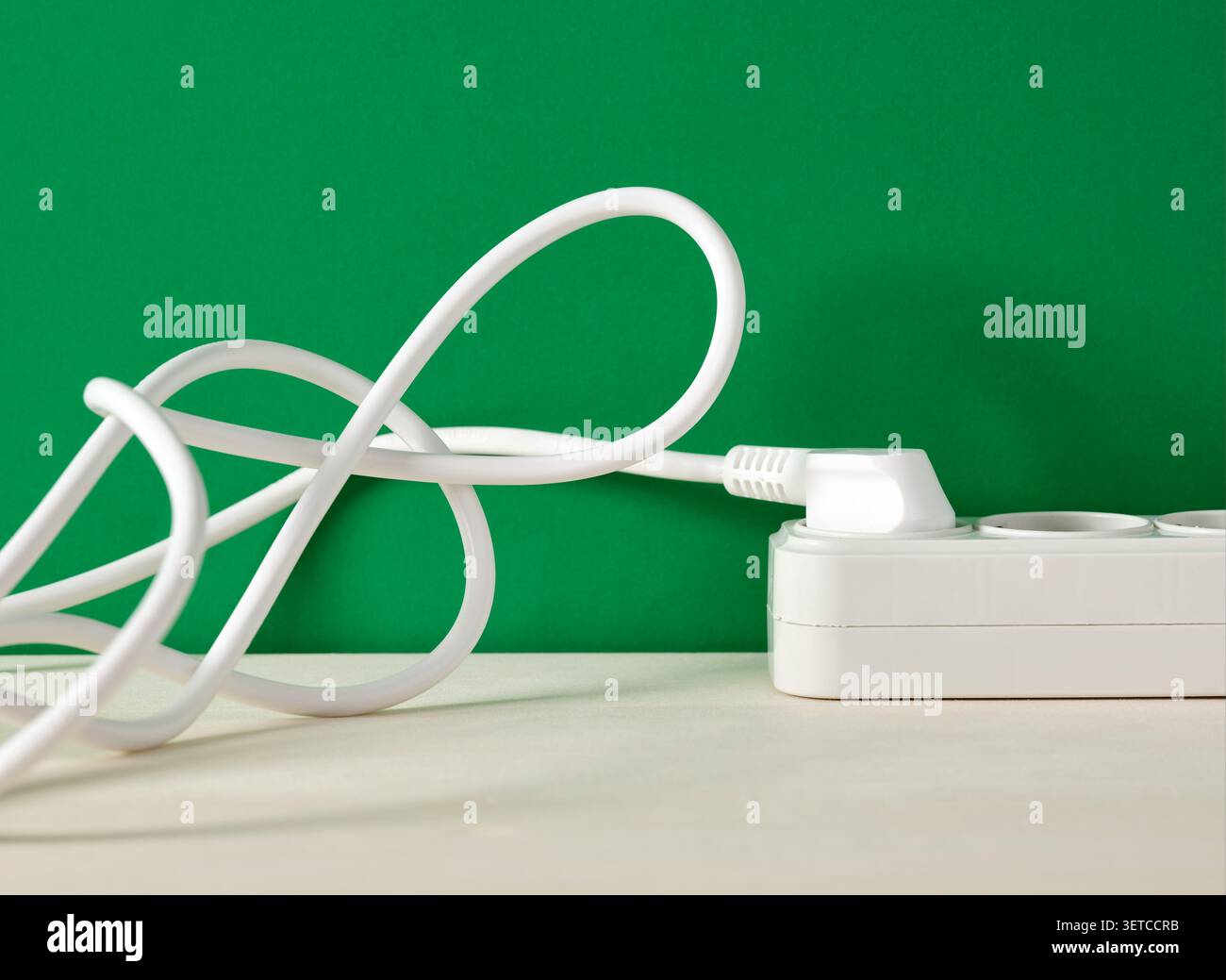 Le câble d'alimentation blanc forme un nœud enchevêtré, branché dans une rallonge blanche sur un fond vert vif Banque D'Images