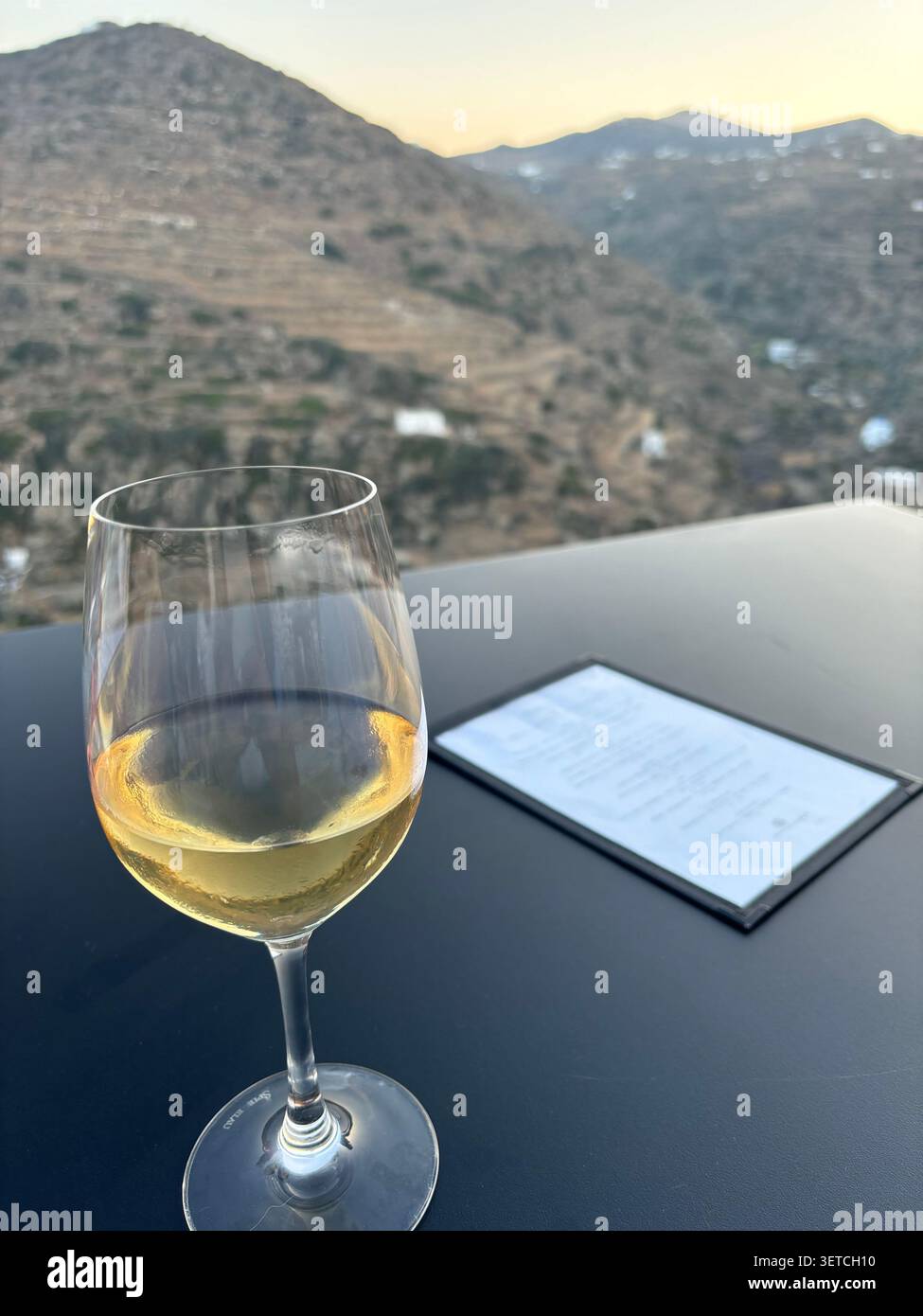 Verre de vin blanc avec vue sur les collines de Kastro, Milos, Grèce. - Image de stock capturée avec un smartphone