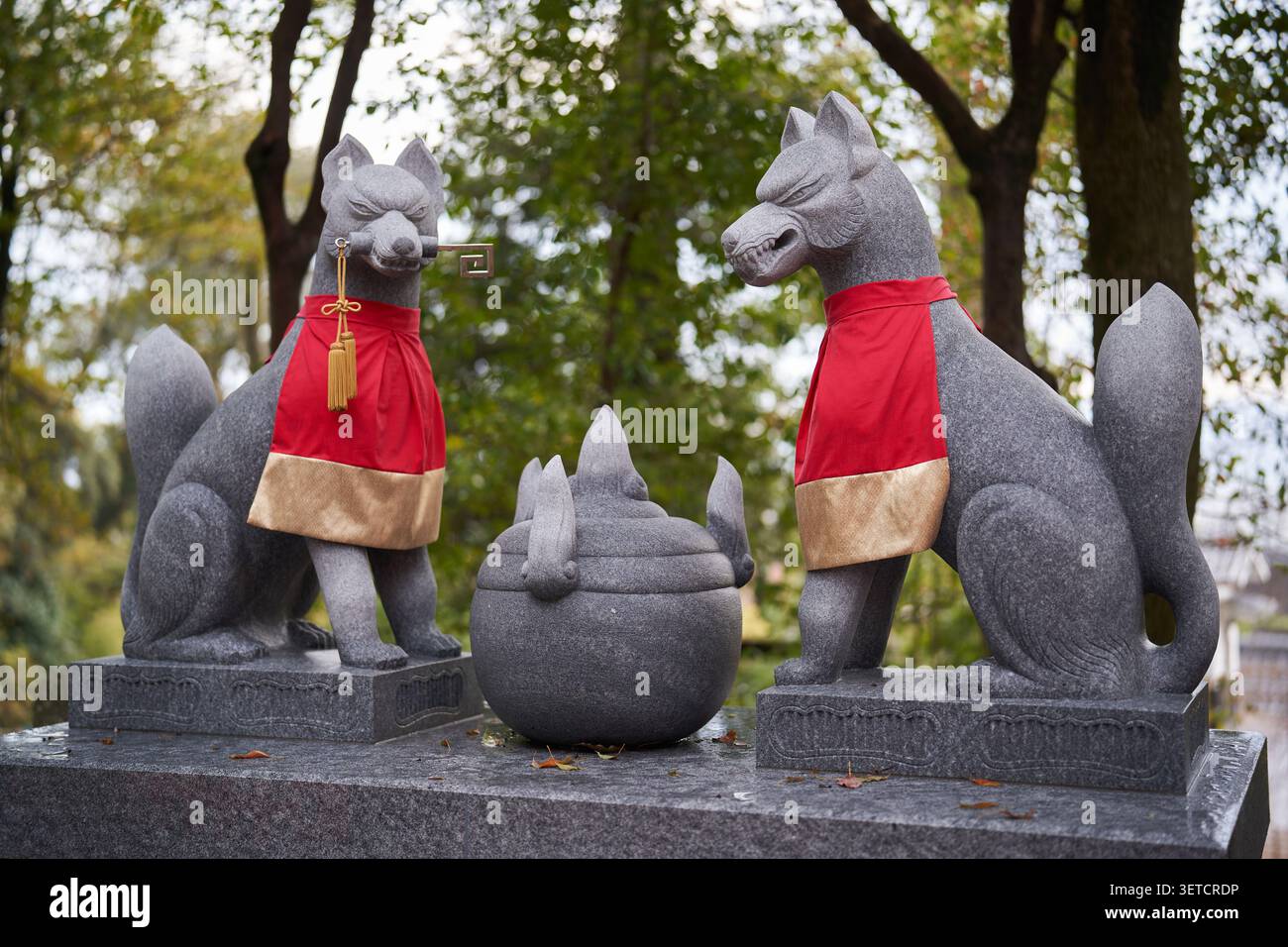 Paire de statues de renard kitsune en granit avec des bavoirs rouges flanquant un bijou dans un sanctuaire Inari de Kyoto Banque D'Images