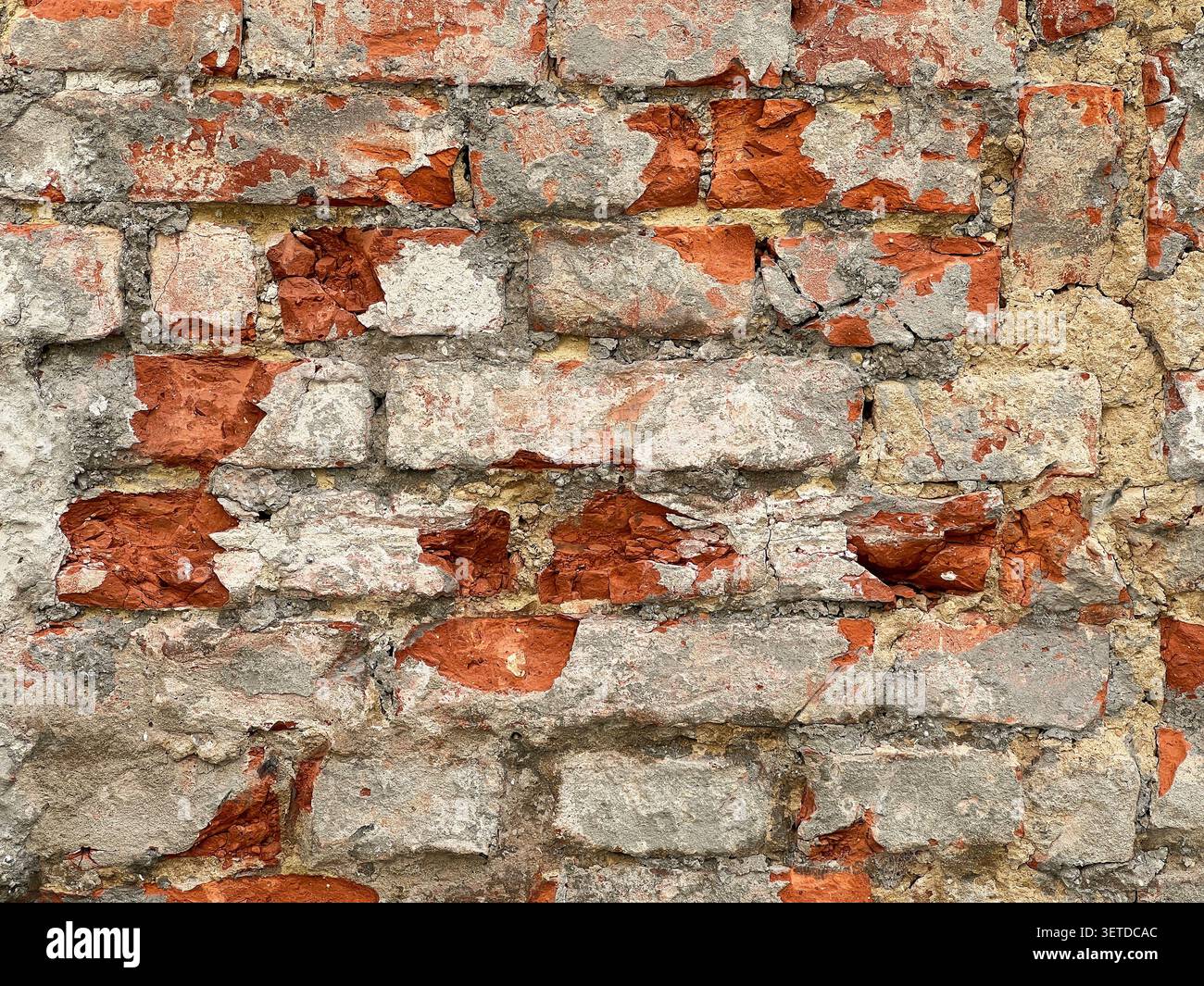 Gros plan d'un vieux mur de briques altérées avec du plâtre fissuré et des briques rouges exposées. Fond rustique de texture de maçonnerie grunge. Banque D'Images