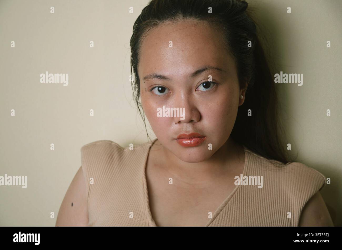 Jeune femme asiatique sérieuse regardant la caméra sur un fond intérieur neutre. Banque D'Images