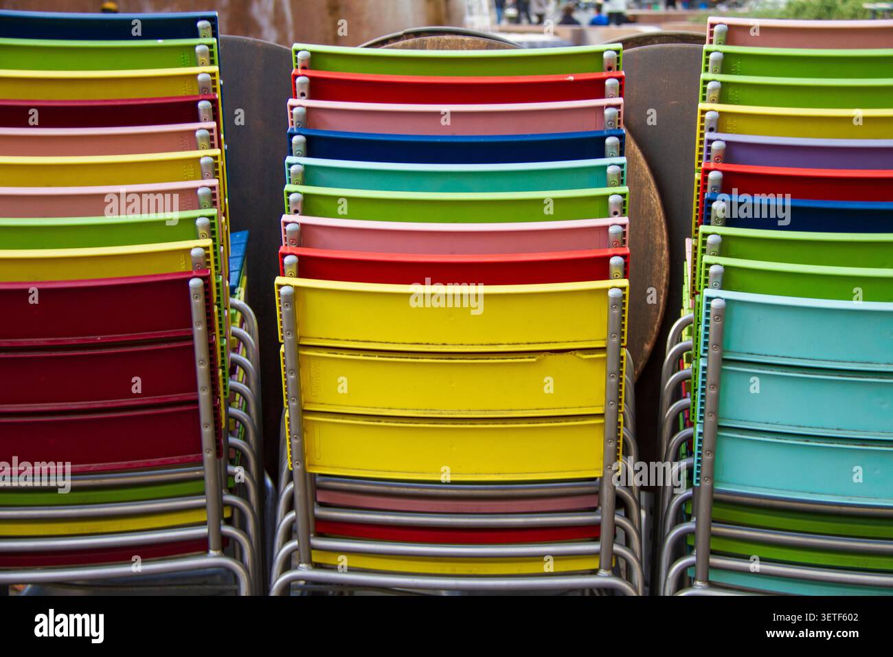 Trois rangées verticales de chaises en métal avec des dossiers en plastique de couleurs vives sont empilées à l'extérieur. Nuances de rouge, jaune, vert, bleu clair et rose A. Banque D'Images