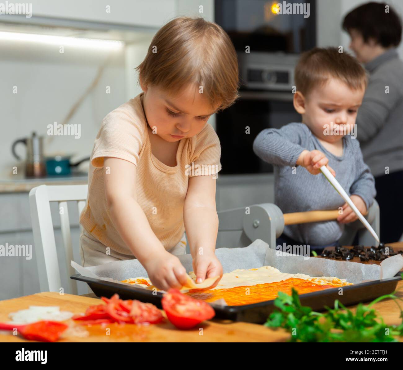 La famille cuisinent la pizza ensemble dans la cuisine à la maison confortable. Les enfants mignons avec une mère heureuse préparent la nourriture ou le repas pour le dîner Banque D'Images