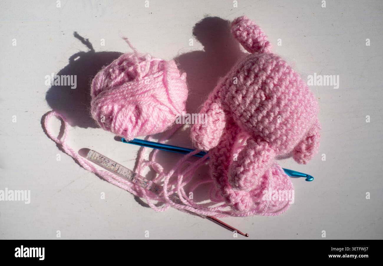 Boules de fil rose, crochet et morceaux de tissu faits à la main non finis sur une surface blanche brillante avec de fortes ombres de jour, montrant le travail artisanal créatif Banque D'Images