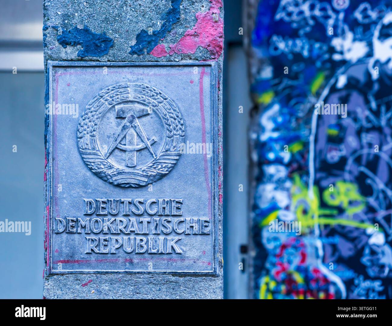 Gros plan de l'emblème de l'État de l'ancienne République démocratique allemande (RDA) avec le mur de Berlin en arrière-plan. Symbole GDR, emblème DDR. Banque D'Images