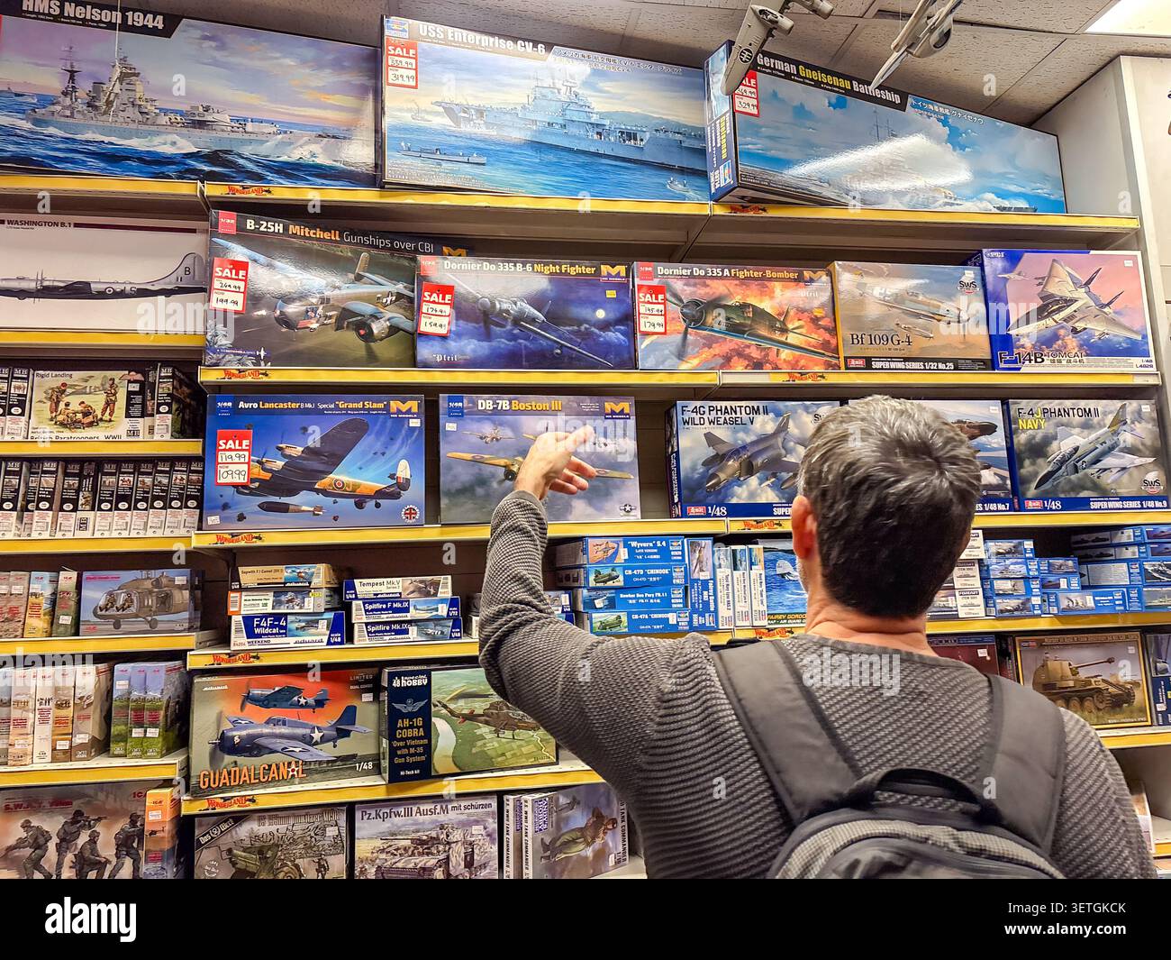Une personne atteignant pour une boîte d'avion modèle réduit sur une étagère de magasin de loisirs remplie de divers kits de modèles en plastique aéronautique et navale. Banque D'Images