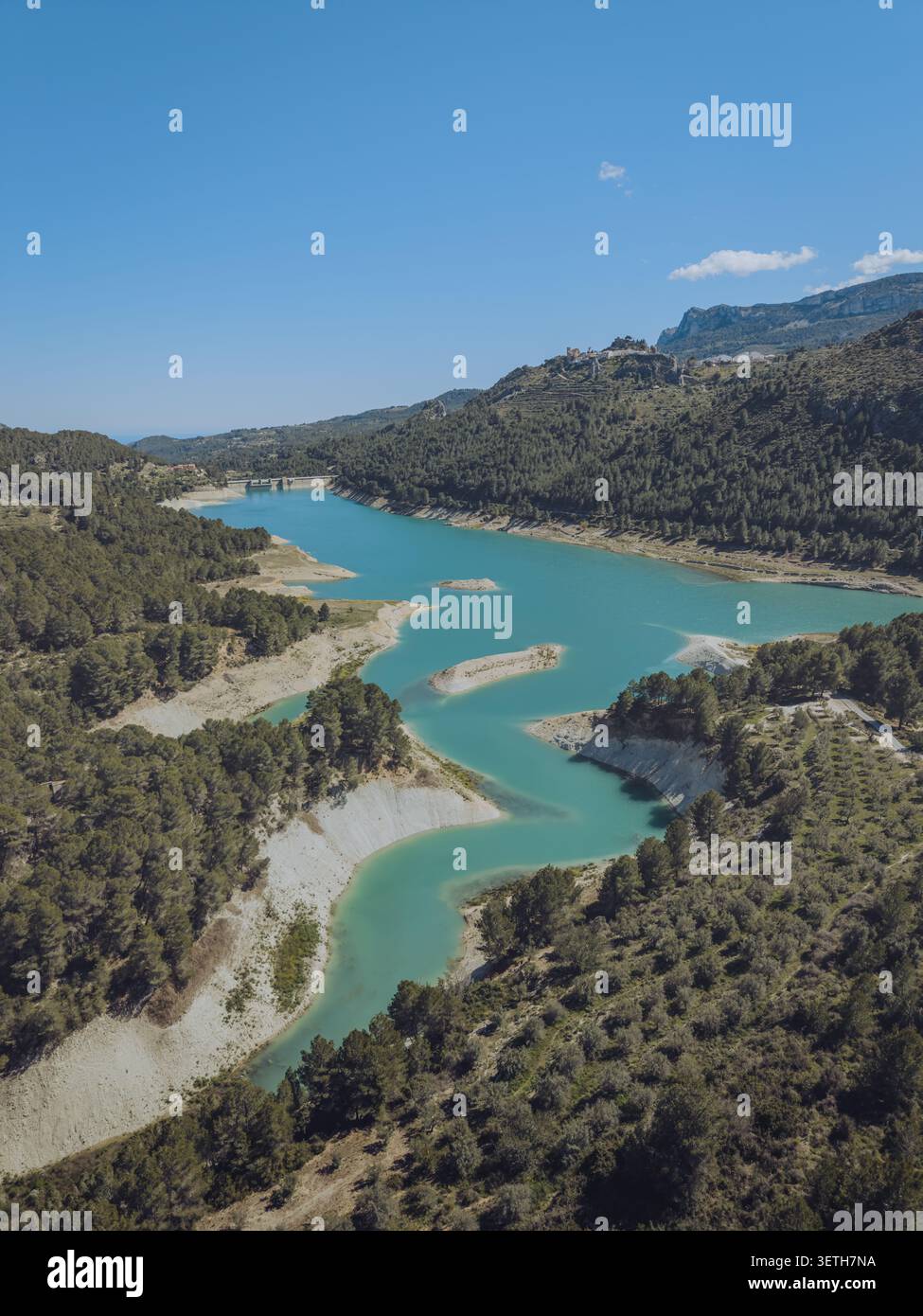 Vue aérienne du réservoir de Guadalest avec de l'eau turquoise entourée de forêts de pins et de collines escarpées sous un ciel bleu clair à Alicante, Valence Comm Banque D'Images