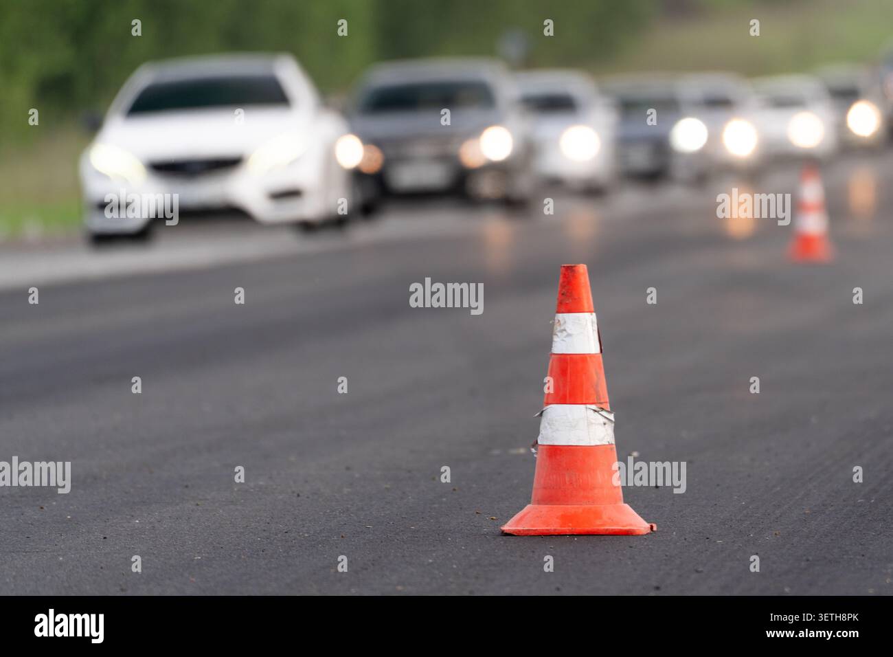 Cônes de circulation marquant une zone de travail sur la route avec une ligne de voitures en arrière-plan. Concept de travaux routiers, fermeture de voie, restriction de circulation, détour, traf Banque D'Images