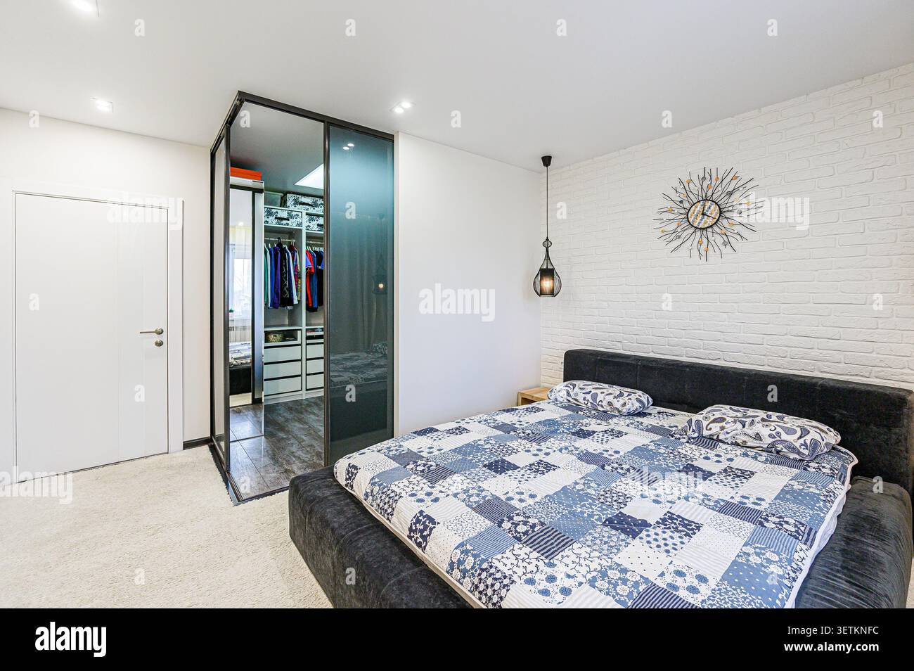 Chambre confortable avec mur de briques blanches, lit couette à motifs, dressing et horloge murale unique Banque D'Images