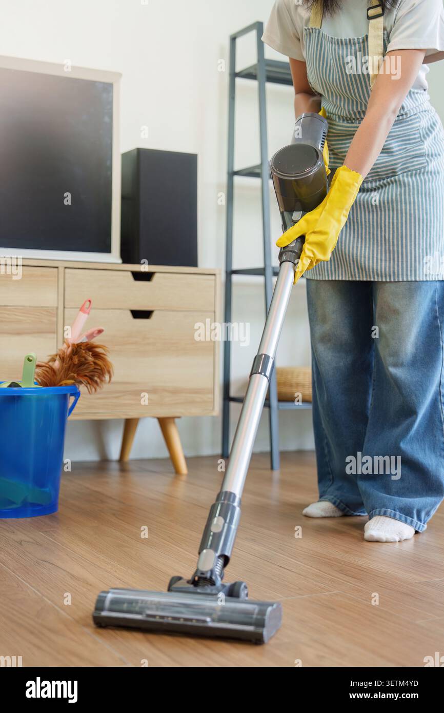 Photo recadrée d'une femme aspirant le plancher en bois avec un aspirateur sans fil Banque D'Images