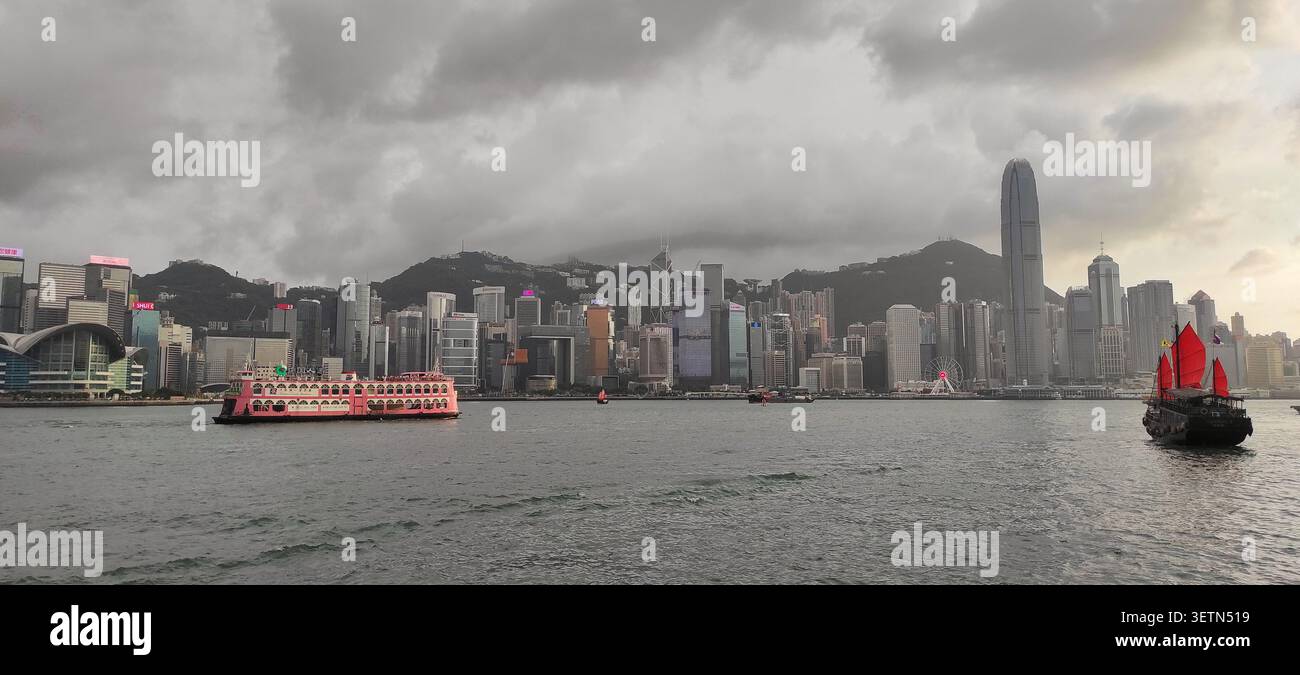 HONG KONG - 18 JUILLET 2023 : un bateau de croisière rose et une jonque à voile rouge traversent le port Victoria au crépuscule. Banque D'Images