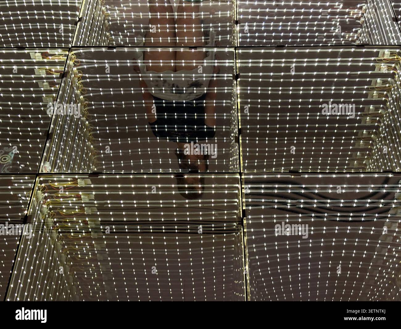 Une personne debout sur une grille de panneaux de verre éclairés créant une illusion optique de profondeur. Newcastle, Angleterre. Banque D'Images