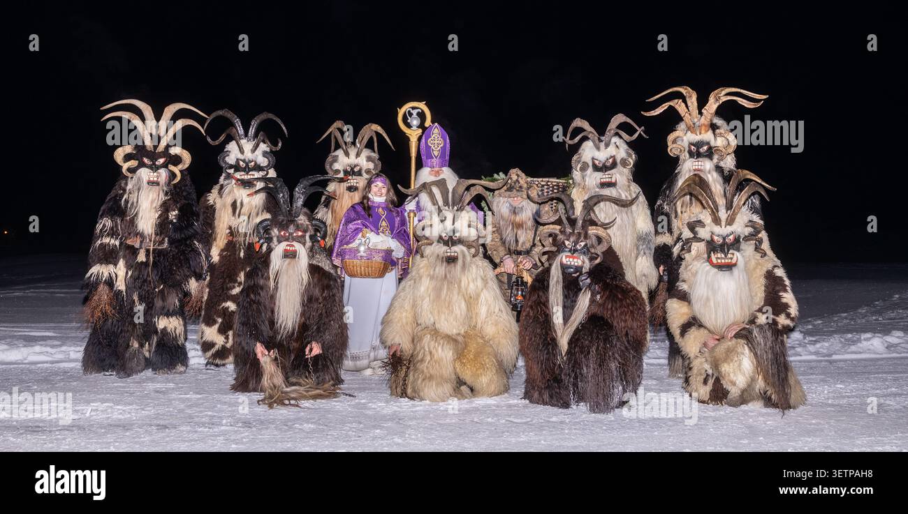 Groupe de personnes vêtues de costumes traditionnels debout sur la neige la nuit lors d'un événement culturel, Bad Gastein, Autriche Banque D'Images