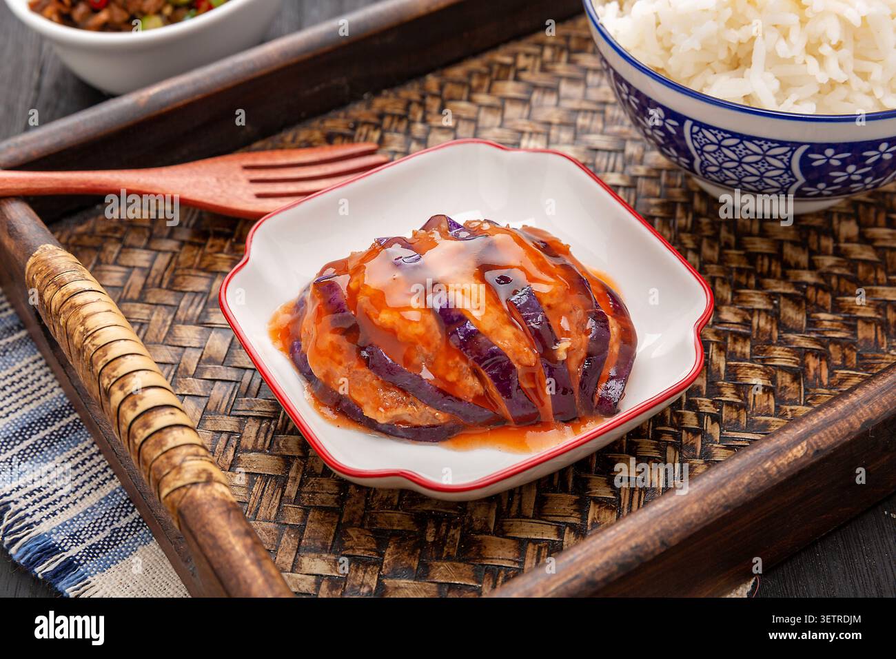 Gros plan d'une seule portion d'aubergine chinoise farcie de lanterne avec sauce salée, servie sur une assiette carrée vintage avec du riz cuit à la vapeur sur un tra de bambou Banque D'Images